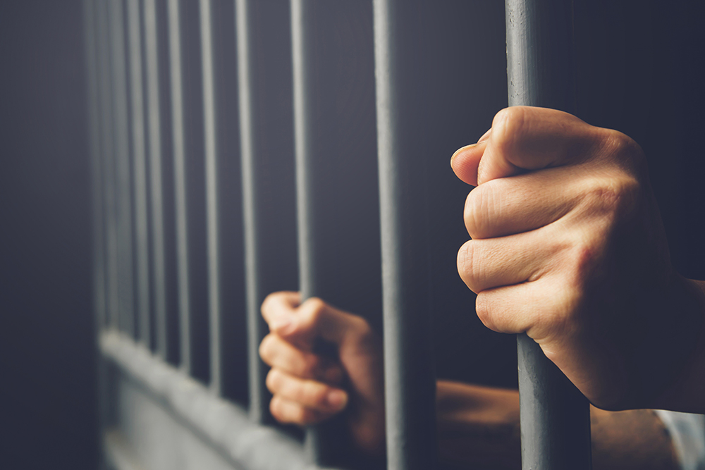 prison hands of behind hold jail bars